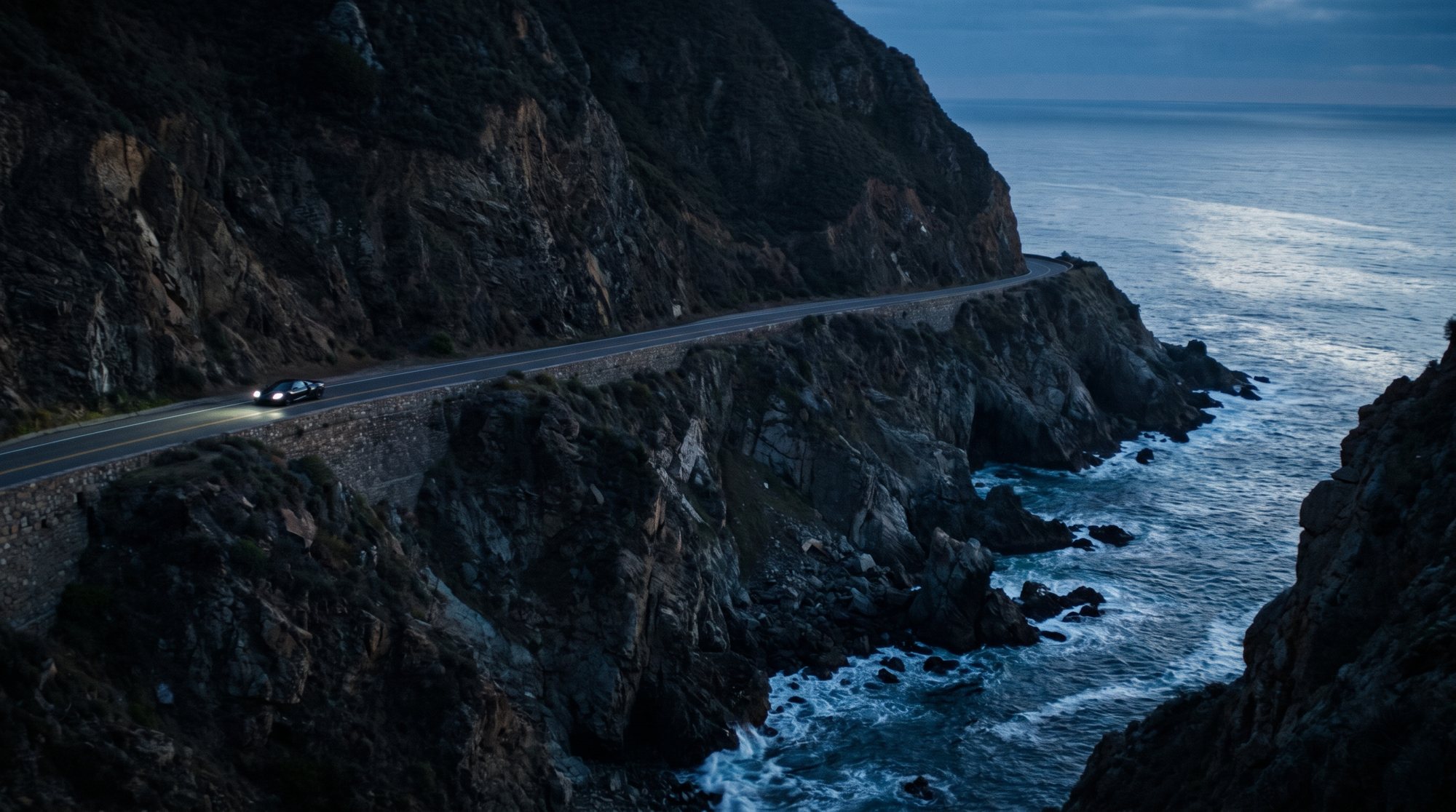 A car on an empty coastal road cut into a cliff