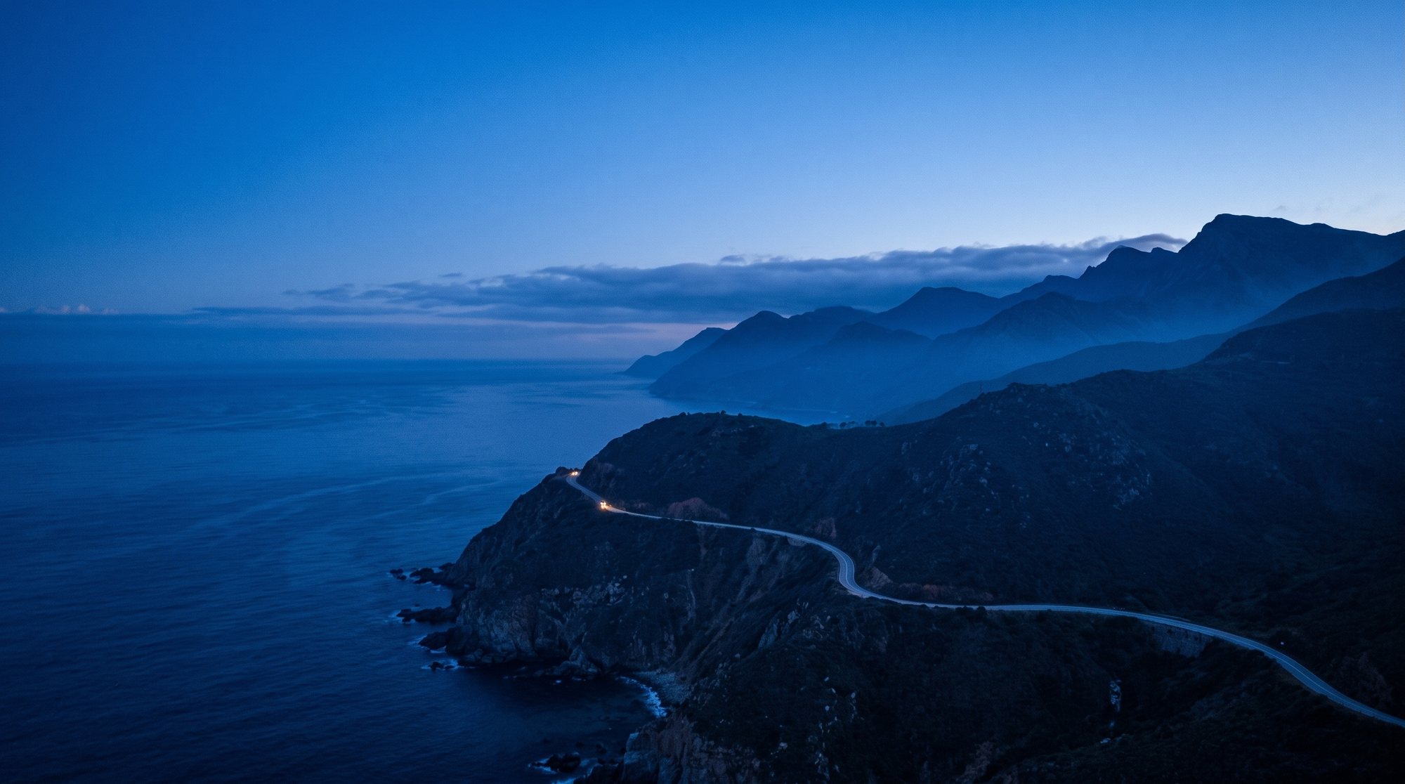 A coastal road as a thin ribbon on a vast cliff at blue hour